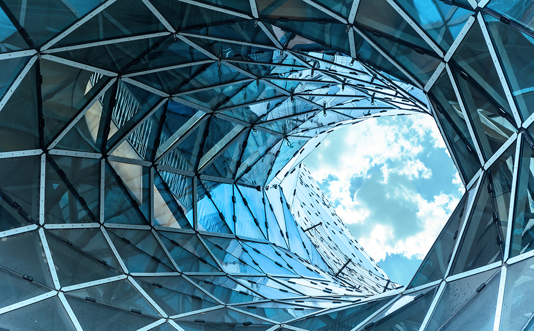 Looking up towards white clouds in blue sky through glass-paneled office building, Strategic Business Group | DXC Technology