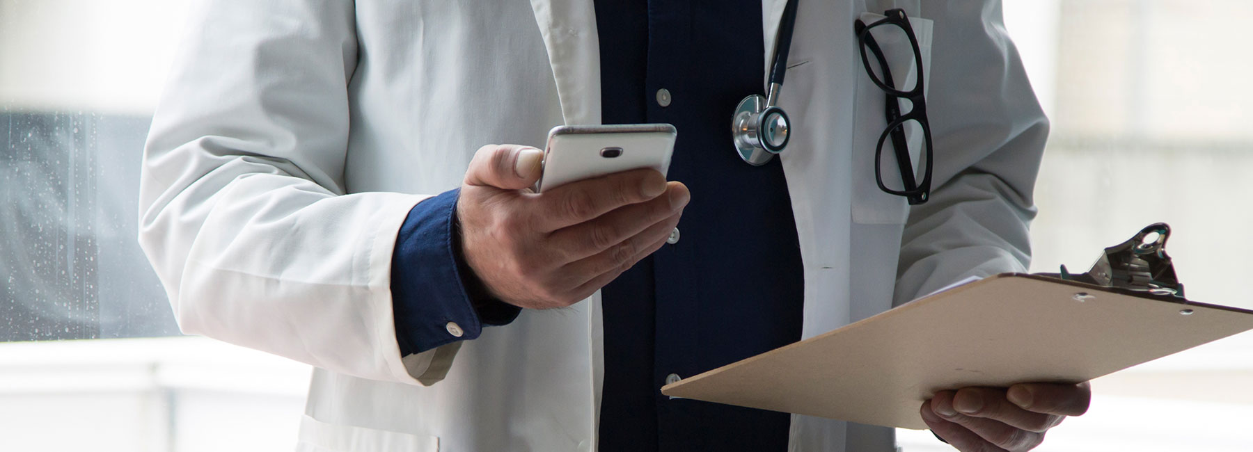Doctor reviewing data on phone and patient chart; AI-powered app for Parkinson’s patients | DXC Technology Customer Story