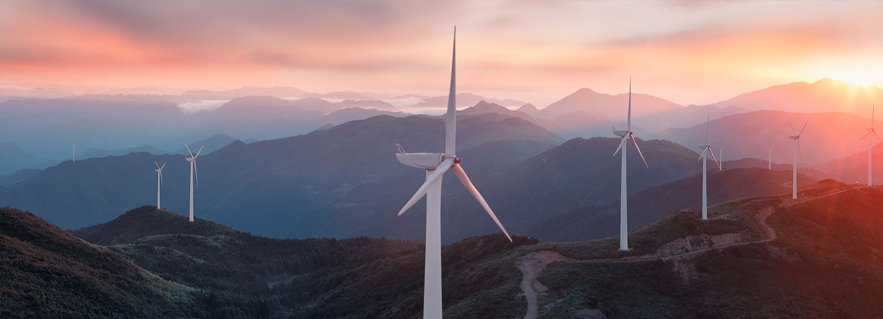 Multiple white wind turbines on top of a mountain range at sunset, Energy, Utilities, Oil & Gas | DXC Technology